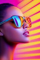 A woman with stylish sunglasses poses against a vibrant, colorful background during sunset photo
