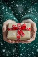 A person holds a beautifully wrapped gift with a red bow while snow falls gently around them photo