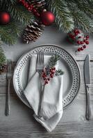Festive holiday table setting with plaid napkin, silver cutlery, and pine cone decoration photo