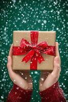 A person holds a beautifully wrapped gift with a red bow while snow falls gently around them photo