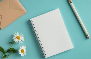 Writing ideas on a blank notepad with a pencil and daisy next to an envelope on a blue surface photo