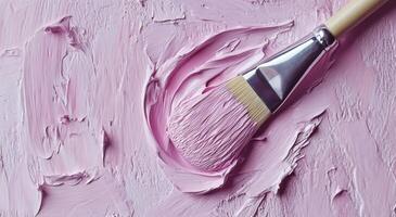 A close-up of a paintbrush applying lavender paint to a textured canvas surface in an art studio photo