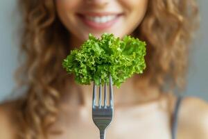 Smiling woman holding fresh green lettuce on fork. World Vegan Day photo