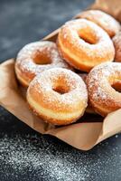 Freshly baked sugary donuts in a rustic brown bag on a dark surface photo