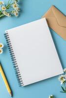 A blank notebook, pencil, flowers, and an envelope positioned on a blue background photo