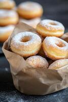 Freshly baked sugary donuts in a rustic brown bag on a dark surface photo