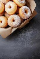 Freshly baked sugary donuts in a rustic brown bag on a dark surface photo