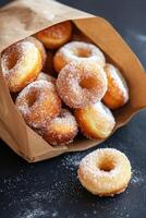 Freshly baked sugary donuts in a rustic brown bag on a dark surface photo