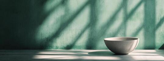Minimalist bowl on a surface casting soft shadows against a green wall in natural light photo