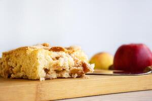 Piece of traditional thanksgiving apple cinnamon pie on the wooden cutting board on the white table, surrounded by fresh apples and walnuts. Autumn dessert. Closeup. Copy space. Top view photo
