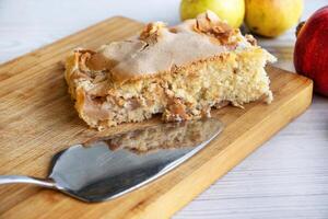 Piece of traditional thanksgiving apple cinnamon pie on the wooden cutting board on the white table, surrounded by fresh apples and walnuts. Autumn dessert. Closeup. Copy space. Top view photo