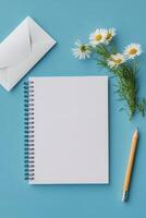 A blank notebook, pencil, flowers, and an envelope positioned on a blue background photo