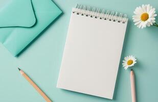 Writing ideas on a blank notepad with a pencil and daisy next to an envelope on a blue surface photo