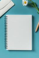 A blank notebook, pencil, flowers, and an envelope positioned on a blue background photo