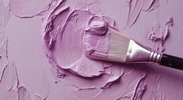 A close-up of a paintbrush applying lavender paint to a textured canvas surface in an art studio photo