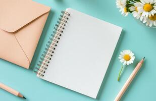 Writing ideas on a blank notepad with a pencil and daisy next to an envelope on a blue surface photo