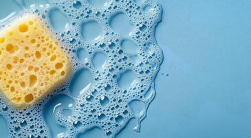 Soapy sponge resting on a blue surface with bubbles scattered around during cleaning activity photo