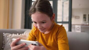 Happy smiling Caucasian child girl carefree daughter playing mobile phone smartphone virtual game online using gaming app at home curious little kid typing screen Internet cyberspace. Gadget addiction video