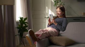 Little girl sitting on sofa mobile phone user smartphone cellphone technology gadget network social media online watching funny laughter humor tapping cyberspace child home device browse website video