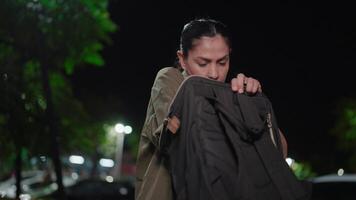 Under the glow of streetlights, a woman search item, A woman is searching through her handbag with a focused expression, revealing a mix of anticipation and uncertainty video