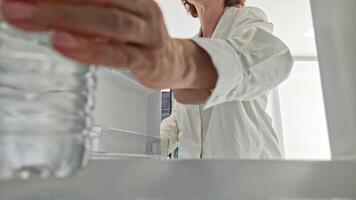 Woman putting small plastic bottle of drinking water in refrigerator to cool, view from inside refrigerator compartment. video