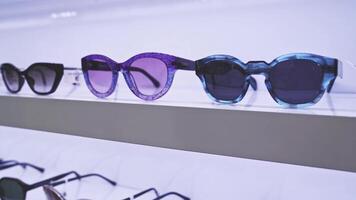 Close-up view of sunglasses on display, modern eyewear design, stylish accessories, retail store setting, fashion choices, diverse colors, organized shelf presentation. video