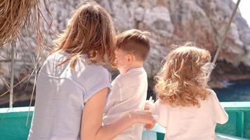 Mother with little son and daughter stands on board ship. They look at mountain they are passing by. Concept of travel, vacation and happy family. video