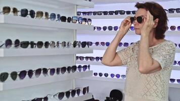 Woman surrounded by sunglasses, trying on frames, browsing stylish options, retail shopping experience, modern interior, assessing personal style, exploring eyewear choices, checking appearance video