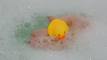 hand holds a rubber yellow duck out of the water in a bath with foam video