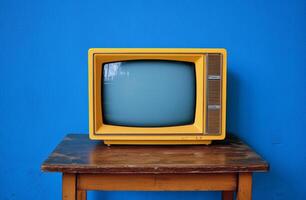 A vintage yellow television sits on a wooden table against a striking turquoise wall photo