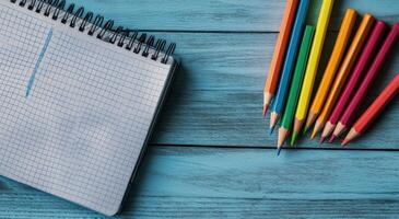 Colorful pencils arranged next to a blank notebook on a blue wooden desk photo
