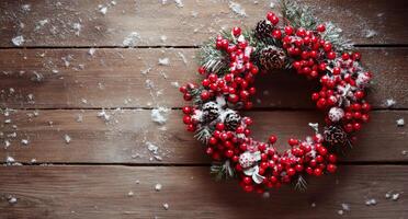 Beautiful winter wreath adorned with red berries and pinecones hanging on a rustic wooden background photo