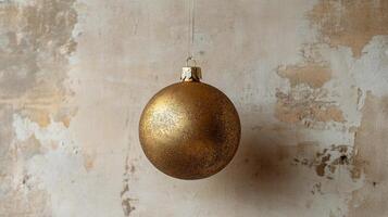 A single golden ornament hanging against a neutral backdrop near the holiday season photo
