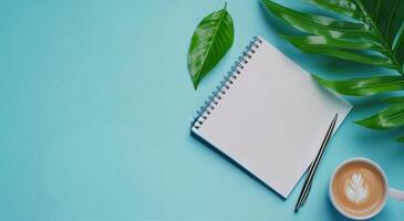 A cozy workspace featuring a coffee cup, a notepad, and a green leaf on a light blue background photo