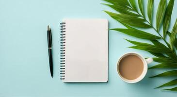 A cozy workspace featuring a coffee cup, a notepad, and a green leaf on a light blue background photo
