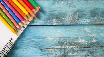 Colorful pencils arranged next to a blank notebook on a blue wooden desk photo