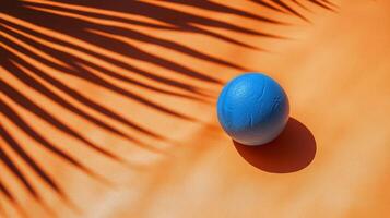 A blue globe on an orange surface with green palm leaves reflecting sunlight in the afternoon photo