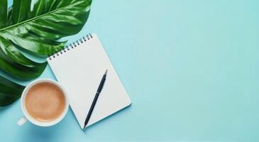 A cozy workspace featuring a coffee cup, a notepad, and a green leaf on a light blue background photo