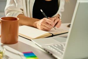 Person is sketching in notebook while working remotely at desk with laptop. Freelance work at home office. Graphic designer drawing sketch photo