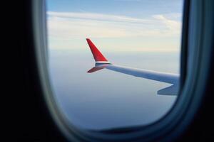 View of airplane wing from passenger window at high altitude above the clouds. Air travel and flight concept photo