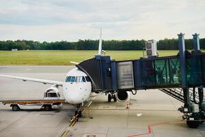 Passenger airplane docked at airport gate with connected jet bridge and ground support vehicle. Passengers boarding white airplane photo