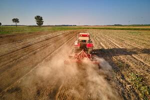 Red tractor working in agricultural field, cultivating and plowing dry soil, aerial view. Agribusiness concept. Small farming concept photo