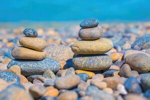 Symbolic scales of stones against the background of the sea and blue sky. Concept of harmony and balance. Pros and cons concept. Pyramid stones balance on the sand of the beach with blurred background photo