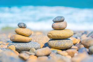 Symbolic scales of stones against the background of the sea and blue sky. Concept of harmony and balance. Pros and cons concept. Pyramid stones balance on the sand of the beach with blurred background photo