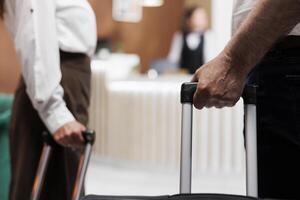 Close-up of a caucasian couple with bags entering foyer of a luxury hotel. View of retired senior customers holding bags as they approach the registration counter to check in with receptionists. photo