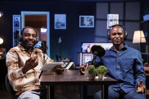 Two black men host a live talk show, discussing various topics while interacting with fans. They use professional microphones to create high-quality content for an online streaming service. photo