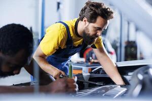 Colleagues in car service use torque wrench to tighten bolts after replacing steering mechanism. Teamworking auto repair shop workers use professional tools to fix customer automobile photo