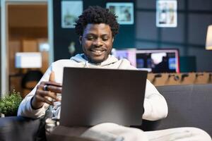 Man feeling excited after receiving salary, adding payment method on website, looking at debit card info. Buoyant self employed man delighted to do online shopping, looking to do acquisitions photo