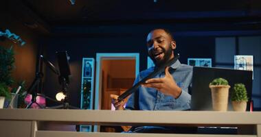Content creator in dimly lit apartment studio films keyboard and mouse set review for online streaming platforms. African american man hosts internet show, unpacking wireless computer peripherals photo