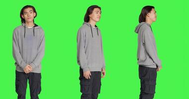 Young guy doing no gesture in studio, expressing negativity and disapproval over isolated greenscreen background. Asian man being displeased and disagreeing with something. photo